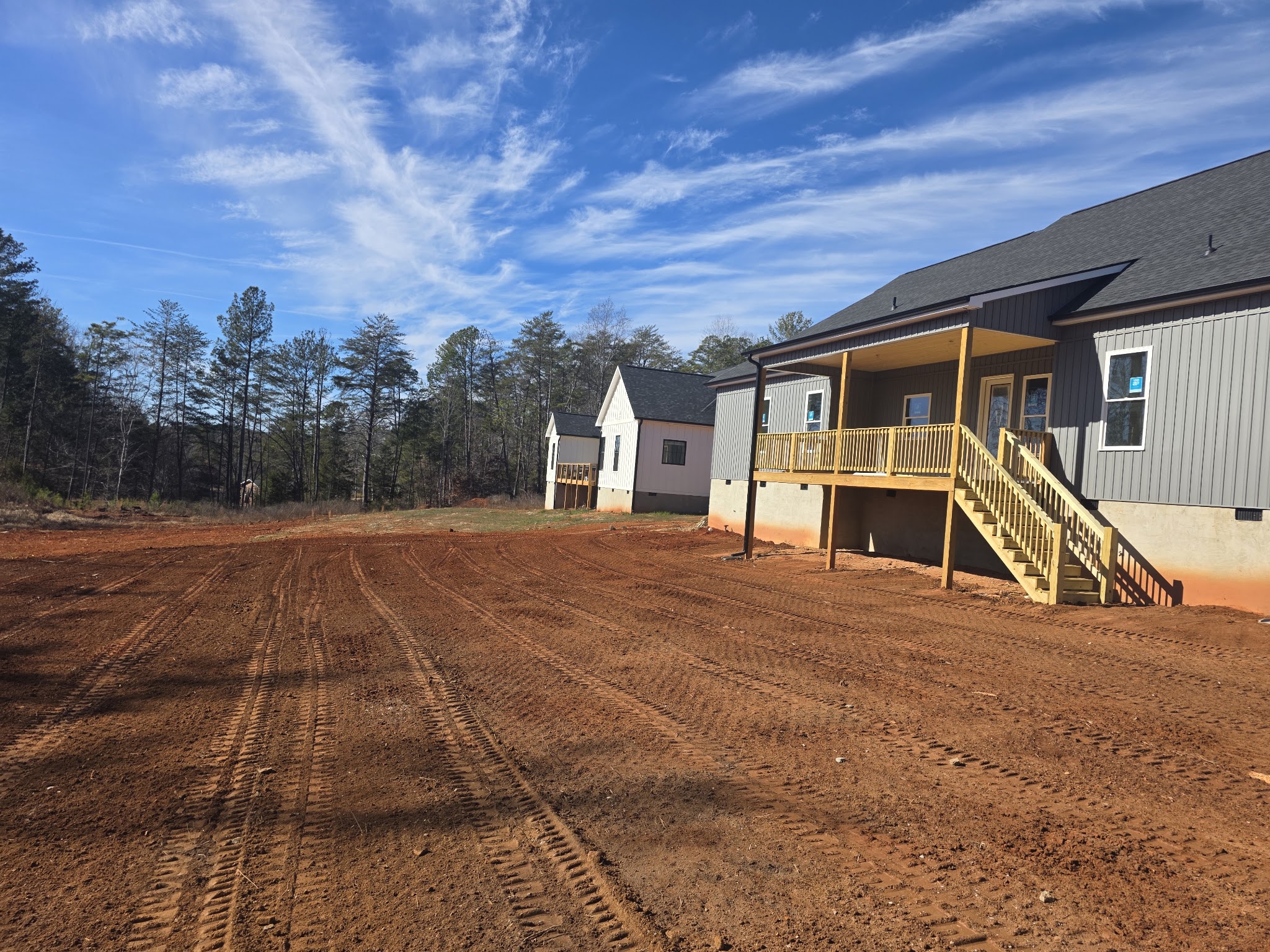 A freshly graded red clay lot beside new homes, tractor tracks still in the soil